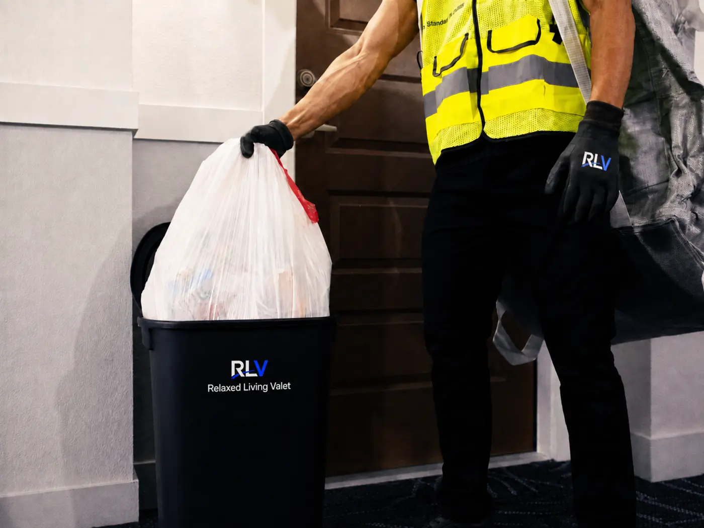 Relaxed Living Valet worker collecting a tied trash bag from a resident’s doorstep bin